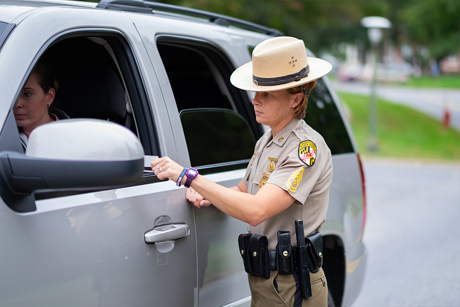 Maryland State Police officer speaking with a driver through a vehicle window during a traffic stop or public safety interaction.