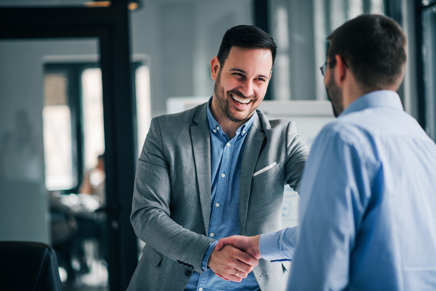 Two professionals shake hands in an office while smiling, suggesting a successful business meeting, partnership, or agreement.