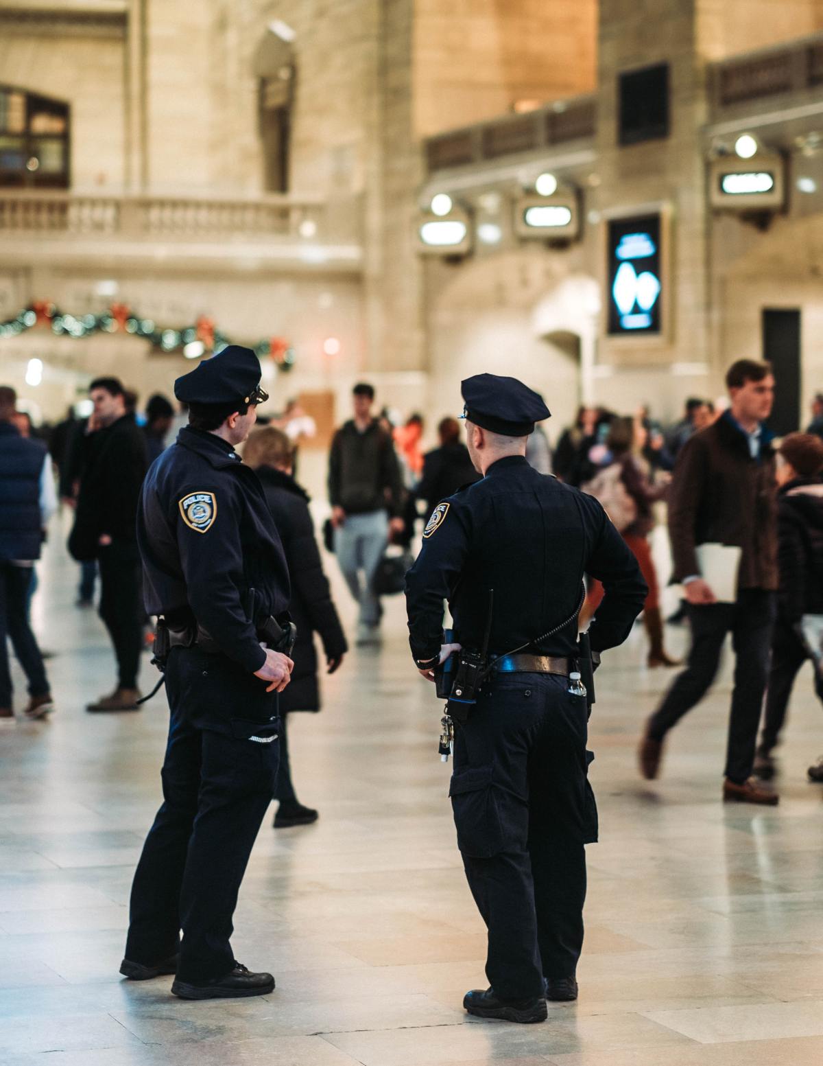 Two uniformed NYPD police officers stand watch in the center of a crowded Grand Central Terminal main concourse.